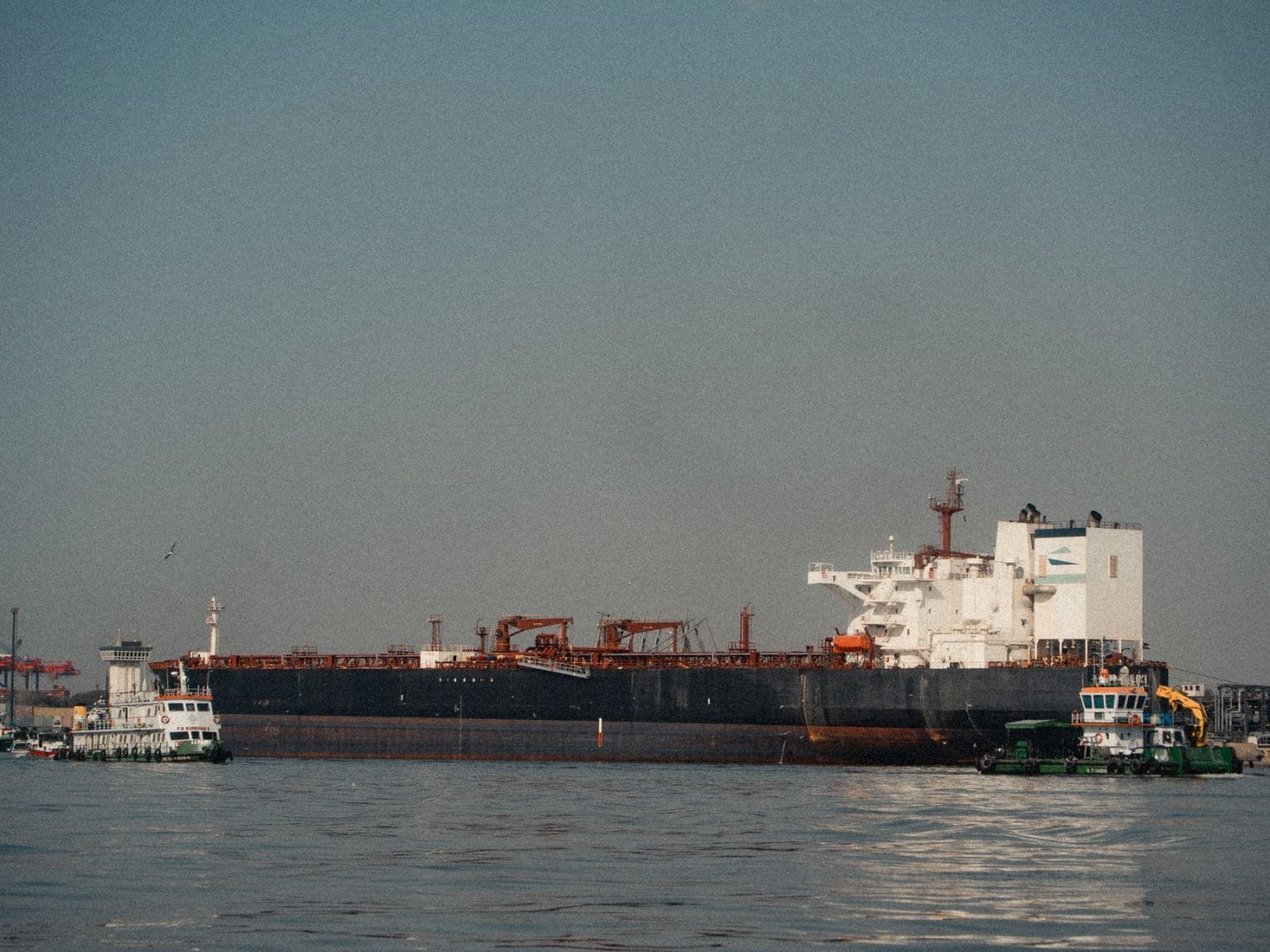 Navio cargueiro atracado em um porto, com rebocadores ao redor em um dia claro.