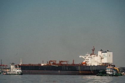 Navio cargueiro atracado em um porto, com rebocadores ao redor em um dia claro.