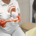 Dentista demonstra a técnica correta de escovação usando um modelo de dentes para uma criança em consultório.