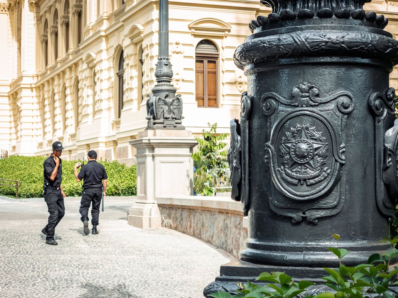Dois agentes de segurança caminham diante de um edifício histórico em São Paulo.