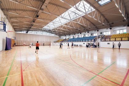Atletas treinam em uma quadra de basquete coberta, em uma arena esportiva.