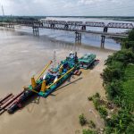 Balsa realiza trabalho de desassoreamento no rio Gorai, próximo a uma ponte em Kushtia, Bangladesh.