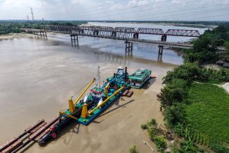 Balsa realiza trabalho de desassoreamento no rio Gorai, próximo a uma ponte em Kushtia, Bangladesh.