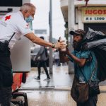 Profissional da Cruz Vermelha presta assistência a um homem em situação de rua ao ar livre.