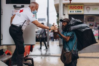 Profissional da Cruz Vermelha presta assistência a um homem em situação de rua ao ar livre.