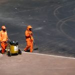 Dois trabalhadores da limpeza urbana usam uniformes laranja enquanto trabalham em uma rua de Brasília.