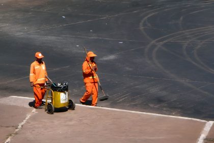 Dois trabalhadores da limpeza urbana usam uniformes laranja enquanto trabalham em uma rua de Brasília.